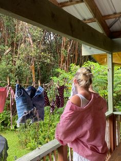 a woman standing on a porch looking at clothes hanging from a line in front of her