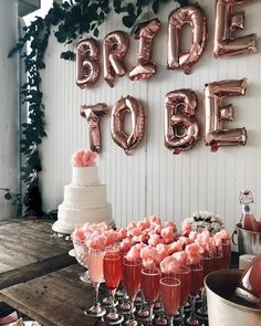 a table topped with lots of pink drinks and balloons in the shape of letters that read bride to be