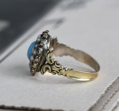 "Circa 1820 an antique Georgian turquoise and pearl halo ring in exquisite condition crafted in 14k gold with a rich buttery glow. Featuring a bright turquoise paste center stone surrounded by natural pearls and tiny faceted jet; such a rare piece, it epitomizes all the romantic charm of the Regency era. Measuring approximately 7/16\" north to south at the center front, tapering through to 2.37 mm at the center back. Size 6 1/4, resizing is not recommended. Paste is essentially a tyoe of leaded Antique Turquoise Ring For Anniversary, Antique Turquoise Ring For Wedding, Antique Turquoise Round Ring For Wedding, Antique Oval Turquoise Wedding Ring, Antique Oval Turquoise Ring For Wedding, Heirloom Style Turquoise Cabochon Wedding Ring, Vintage Yellow Gold Turquoise Ring For Wedding, Antique Round Turquoise Wedding Ring, Antique Style Turquoise Wedding Ring With Cabochon