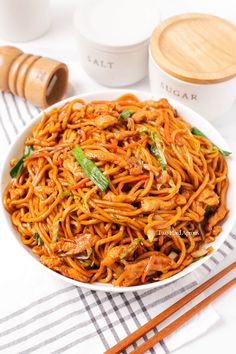 a white bowl filled with noodles next to chopsticks