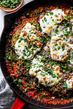 an iron skillet filled with meat and cheese covered in parmesan sauce, garnished with fresh herbs