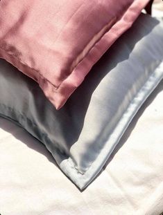 two pillows sitting next to each other on top of a white bed sheet covered in pink and grey sheets