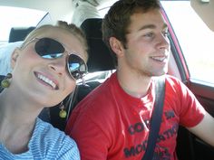 a man and woman sitting in the back seat of a car, smiling at the camera