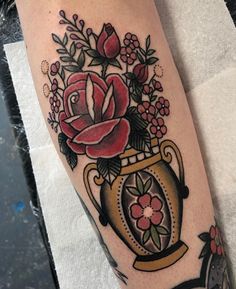 a close up of a person's leg with tattoos on it and flowers in a vase