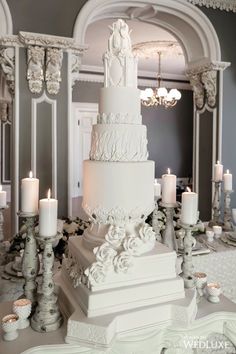 a large white wedding cake sitting on top of a table next to candles and chandeliers