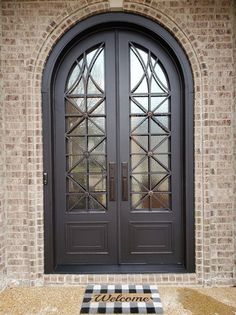 the front door to a brick building with two double doors and a welcome mat on the ground