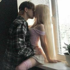 a man and woman kissing in front of a window with long blonde hair on the windowsill