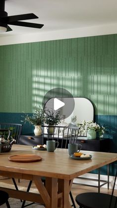 a dining room with green walls and wooden table in front of black chairs, potted plants on top of the table