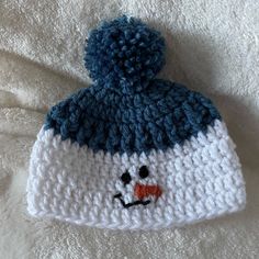 a white and blue knitted hat with a smiling face on the front, sitting on a bed