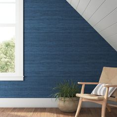 an empty chair in front of a blue wall with a window and potted plant