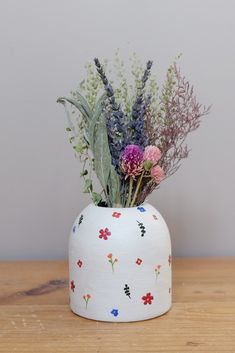 a white vase filled with flowers on top of a wooden table