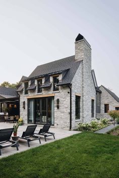 an outdoor patio with chairs and tables in front of a stone house, surrounded by lush green grass