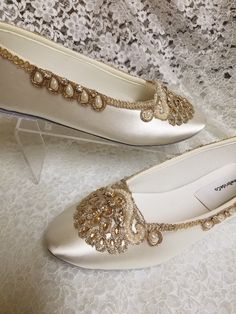 a pair of white shoes with gold beading on the bottom and side, sitting on a lace covered surface