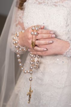 a close up of a person wearing a wedding dress and holding a rosary on their arm