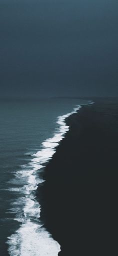 an airplane flying over the ocean on a dark day with waves coming in to shore