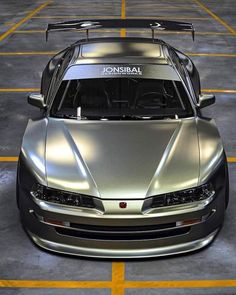 a silver sports car is parked in a parking lot with its hood open and the front lights on