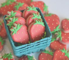 some strawberries are in a blue basket and on the table is cookies with green icing