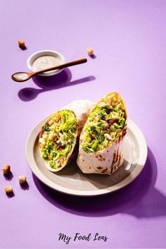 two burritos sitting on a plate next to a spoon