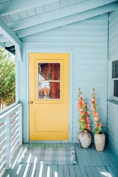 two vases with flowers sit on the porch next to a yellow door and window