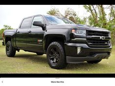 a black truck parked on top of a grass covered field in front of some trees