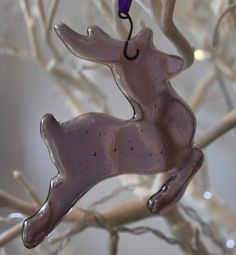 a glass ornament shaped like a deer hanging from a tree with lights in the background