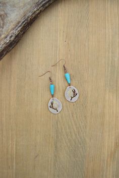 a pair of earrings sitting on top of a wooden table next to a piece of wood