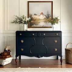 a black dresser sitting next to a painting on the wall in a room with white walls