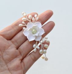 a hand holding a white flower and pearls brooch