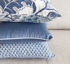 three pillows stacked on top of each other in front of a couch with blue and white patterns