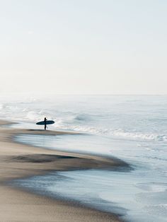 a person holding a surfboard walking on the beach near the ocean with waves coming in