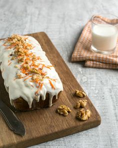 a loaf of carrot bread with icing and walnuts on a cutting board next to a glass of milk