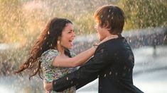 a man and woman dancing in the rain with their arms around each other as they look at each other