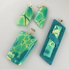 three pieces of jewelry sitting next to each other on a white surface with green and yellow designs