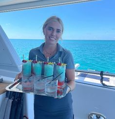 a woman holding a tray with drinks on it in front of some water and blue sky