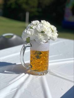 a beer mug filled with white flowers sitting on top of a plastic tablecloth covered table