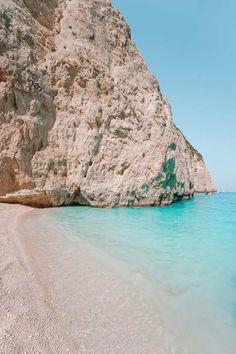 the water is crystal blue and clear at this beach near an enormous rock formation in the ocean