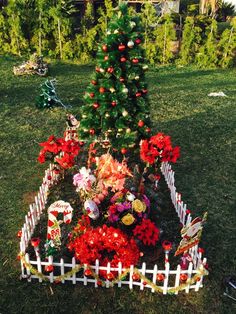 a small christmas tree in the middle of a yard with flowers and decorations around it