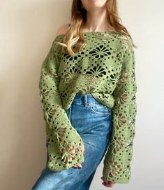 a woman wearing a green crochet sweater and jeans posing for the camera with her hands in her pockets