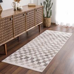 a white rug on top of a wooden floor next to a dresser and potted plant