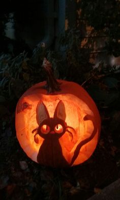 a pumpkin carved to look like a cat with glowing eyes and ears, sitting on the ground