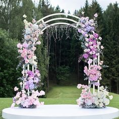 an outdoor wedding ceremony setup with flowers on the arch and greenery in the background