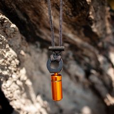 an orange glass bottle hanging from a metal chain on a rock face with a black cord