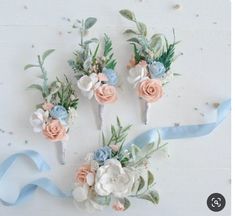 four flower hair pins with blue ribbon on white table top next to flowers and leaves