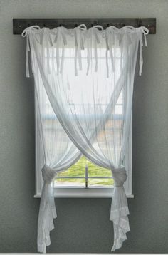 a window with white sheer curtains hanging from it's side