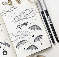 an open notebook with rain and umbrellas on it next to some pens, markers and pencils