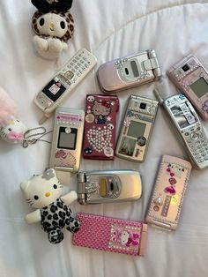 there are many different cell phones on the bed with hello kitty keychains next to them