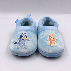 a pair of blue slippers with cartoon characters on the front and back, sitting on a white surface