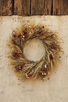 a dried wreath hanging on the side of a wooden wall with red and white flowers