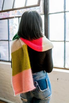 a woman standing in front of a window wearing a multicolored knitted scarf