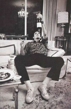 a man sitting on top of a couch holding up a bottle in his right hand